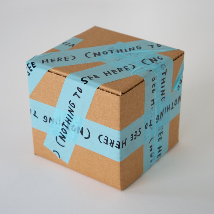 Cardboard box wrapped in Blue packing tape that reads "NOTHING TO SEE HERE" in Adam JK's signature handwriting