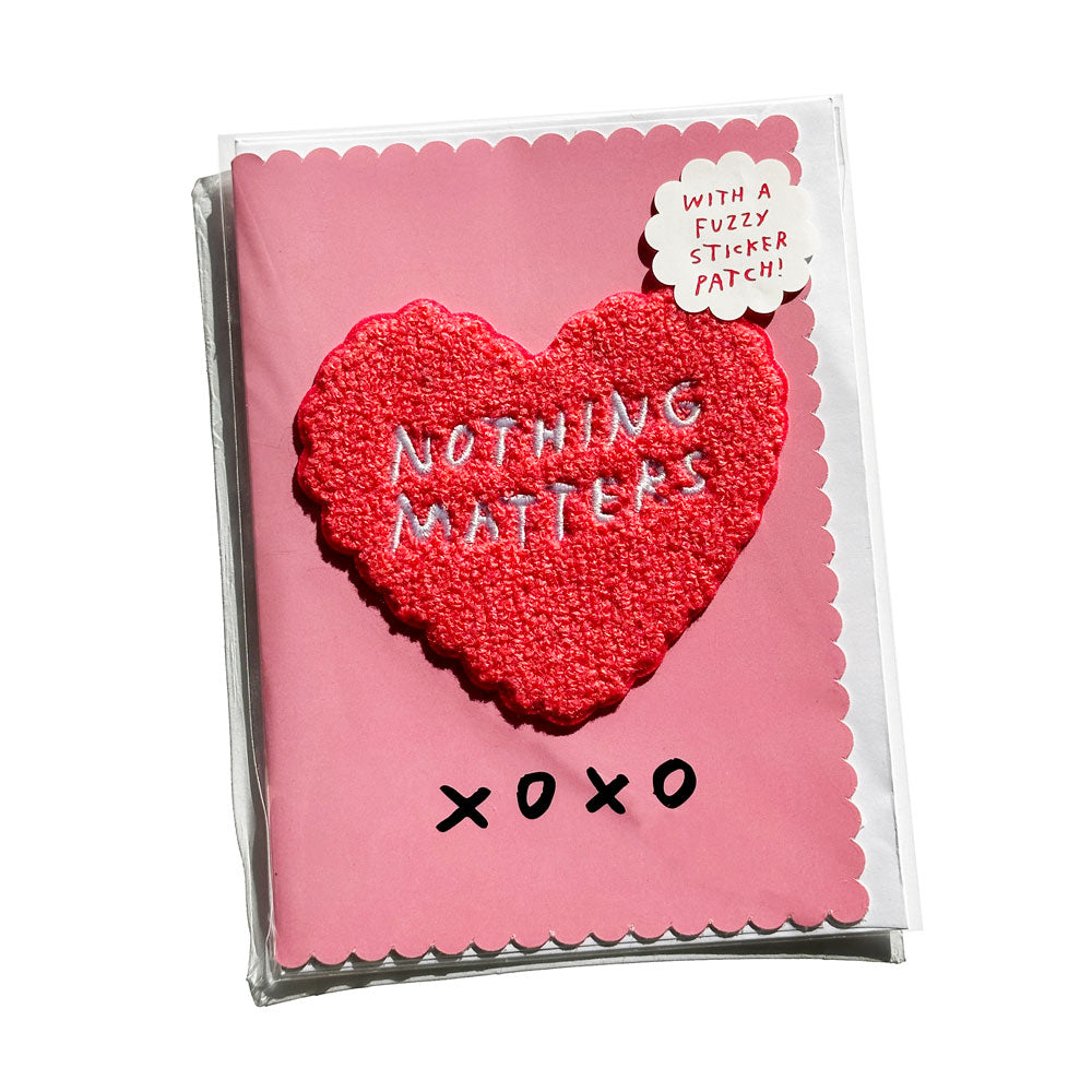 Pink greeting card has removable heart-shaped chenille patch. Patch reads "NOTHING MATTERS" in handwritten text. By Adam JK.