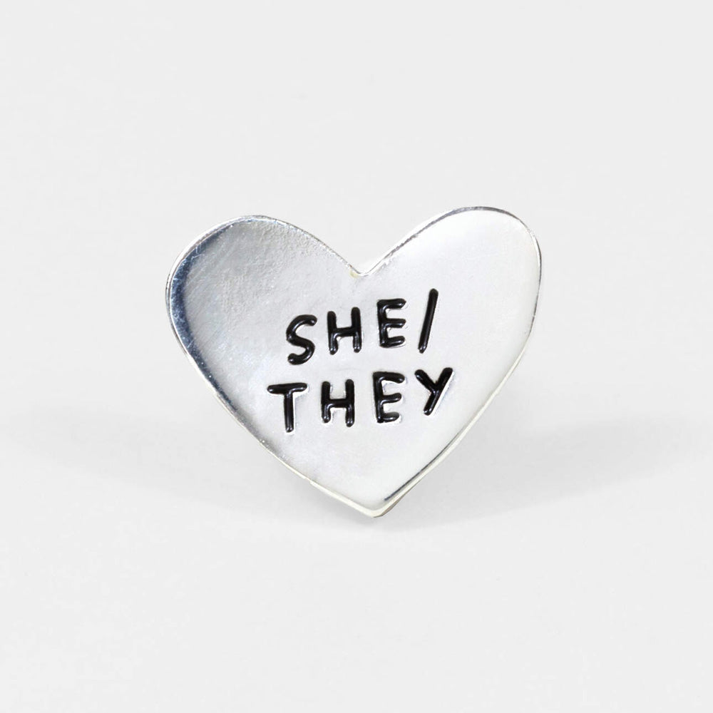 Pronoun Pins by Adam JK – Silver heart reads SHE/THEY